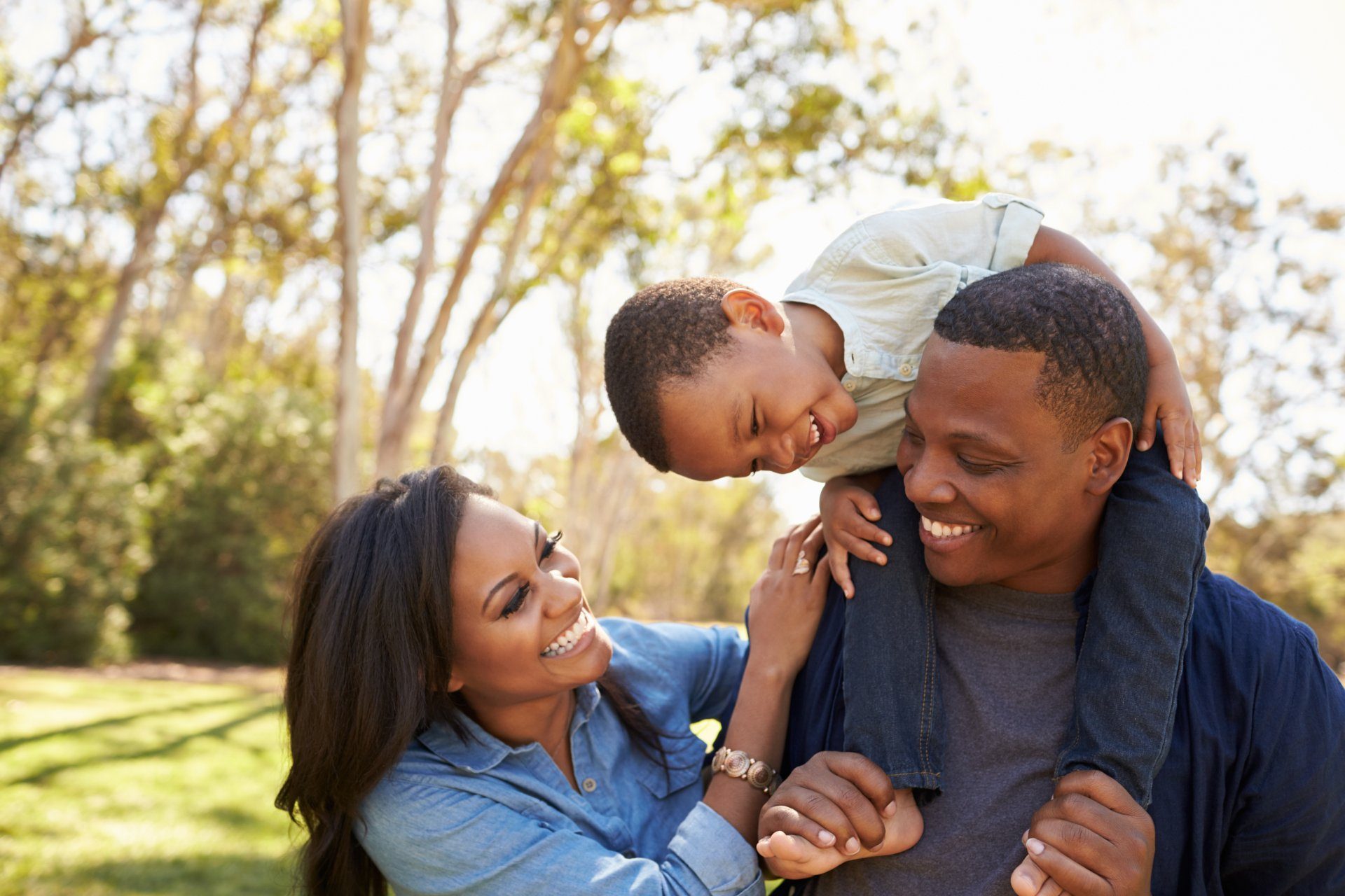 Parents walking through a park with their young son riding on his father’s shoulders