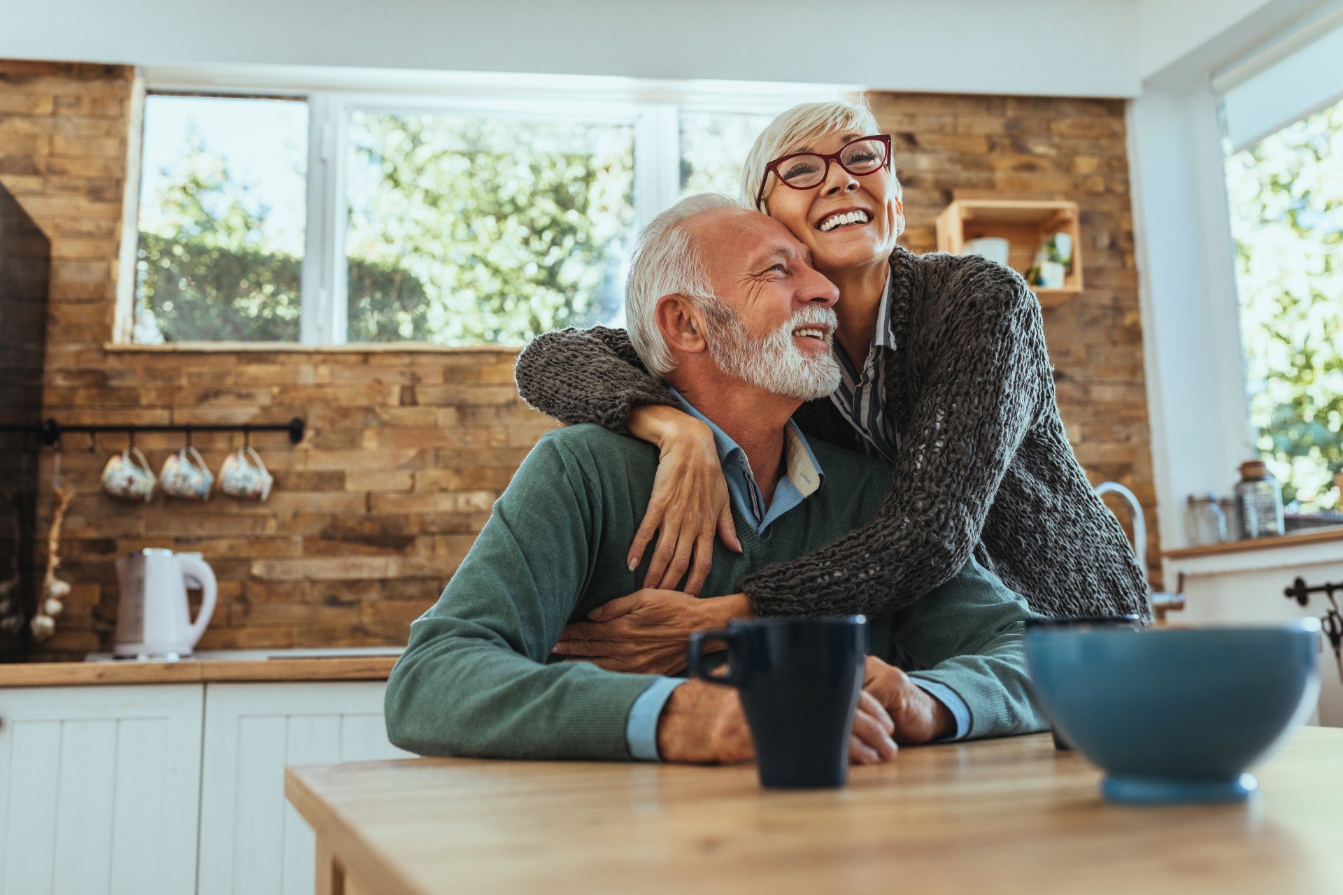 An older couple standing together in their kitchen with morning coffee